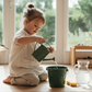 A child pouring water from a green watering can into a green bucket